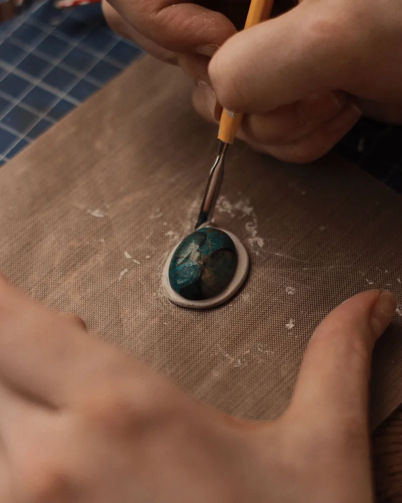 Manos trabajando una pieza de metal pequeña sobre la mesa de taller con herramienta fina